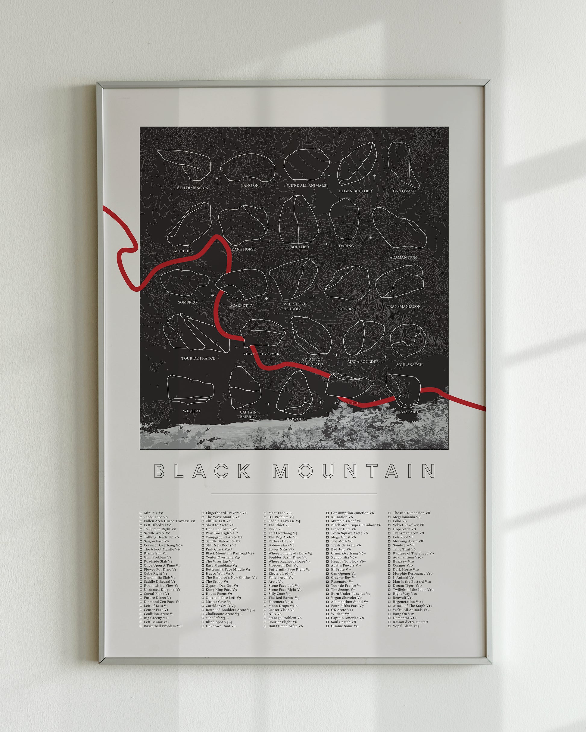 A black color, customized rock climbing ticklist poster for the Black Mountain rock climbing location in San Jacinto Mountain, California. The design has an overlay of crag topography, nature landscapes, and traced boulders, the person's name, and a list of bouldering problems at the bottom. Displayed as wall art in a living room.