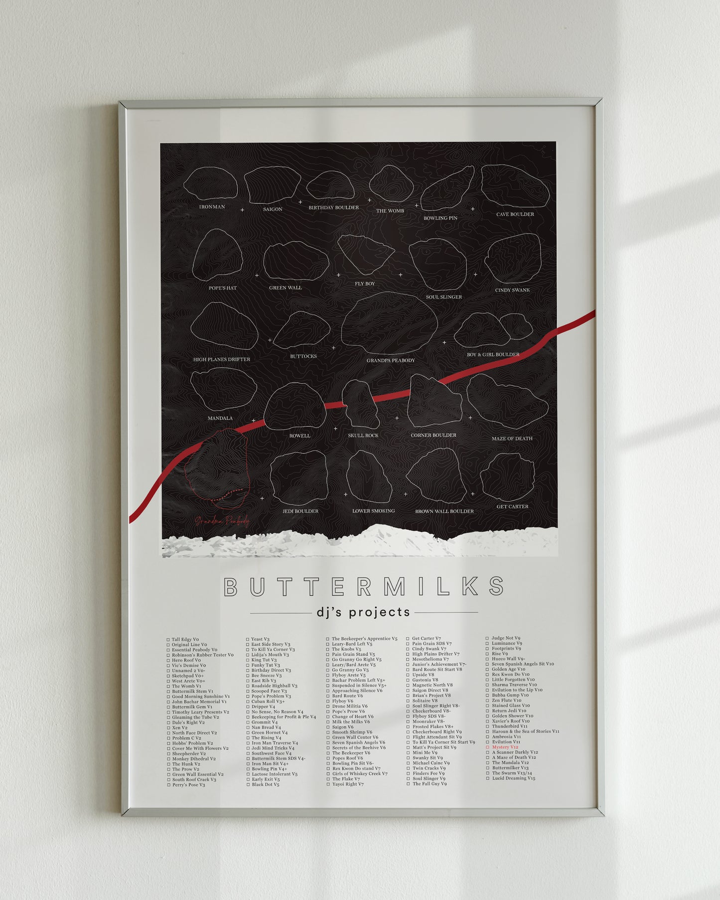 A black color, customized rock climbing ticklist poster for the Buttermilks rock climbing location in Bishop, California. The design has an overlay of crag topography, nature landscapes, and traced boulders, the person's name, and a list of bouldering problems at the bottom. Displayed as wall art in a living room.