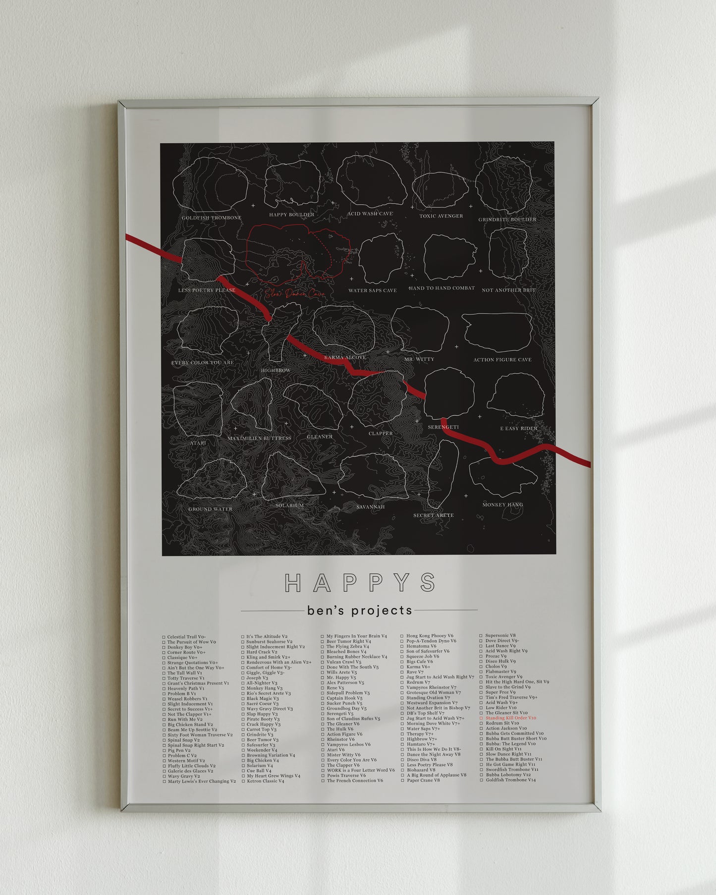 A black color, customized rock climbing ticklist poster for the Happys rock climbing location in Bishop, California. The design has an overlay of crag topography, nature landscapes, and traced boulders, the person's name, and a list of bouldering problems at the bottom. Displayed as wall art in a living room.
