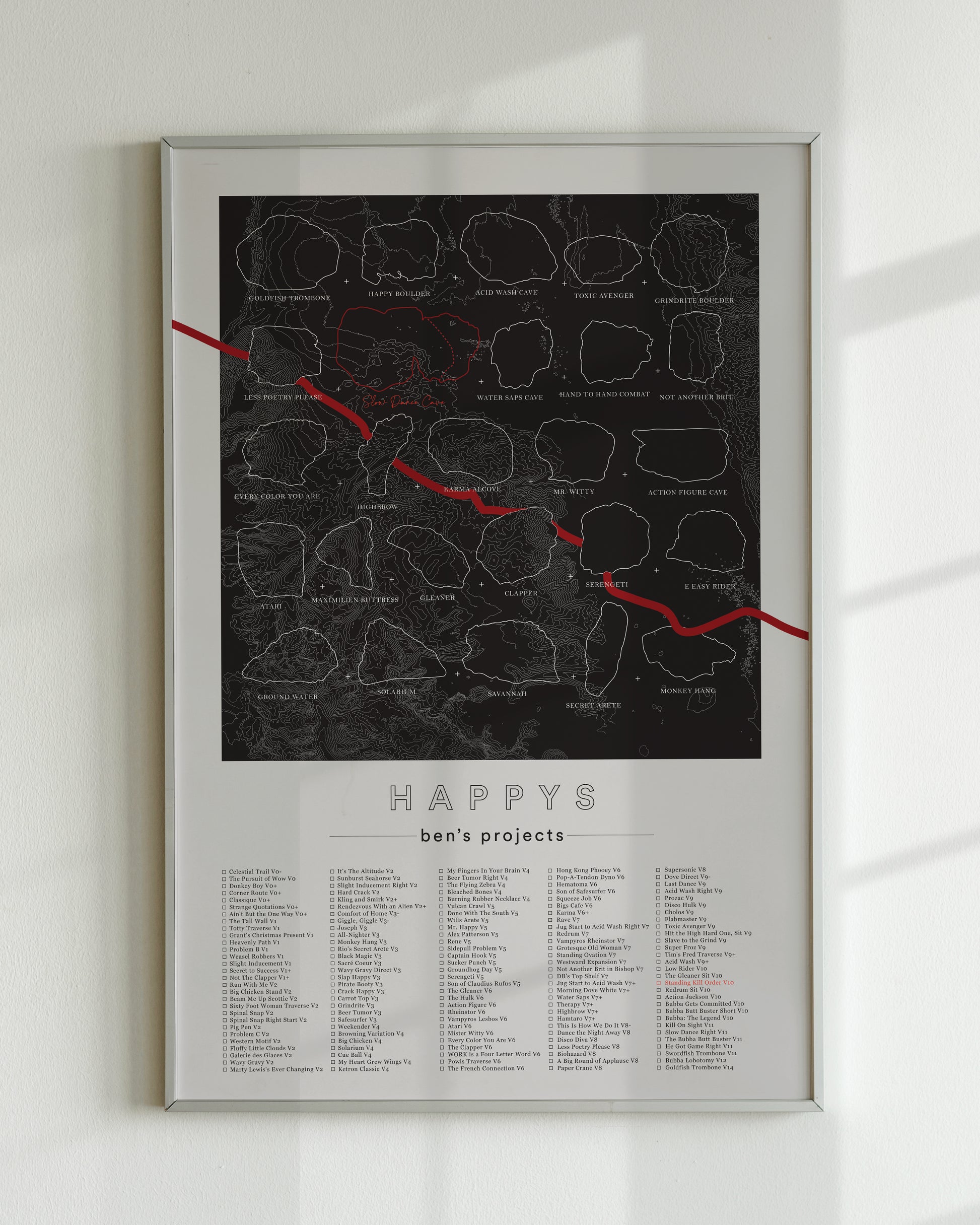 A black color, customized rock climbing ticklist poster for the Happys rock climbing location in Bishop, California. The design has an overlay of crag topography, nature landscapes, and traced boulders, the person's name, and a list of bouldering problems at the bottom. Displayed as wall art in a living room.