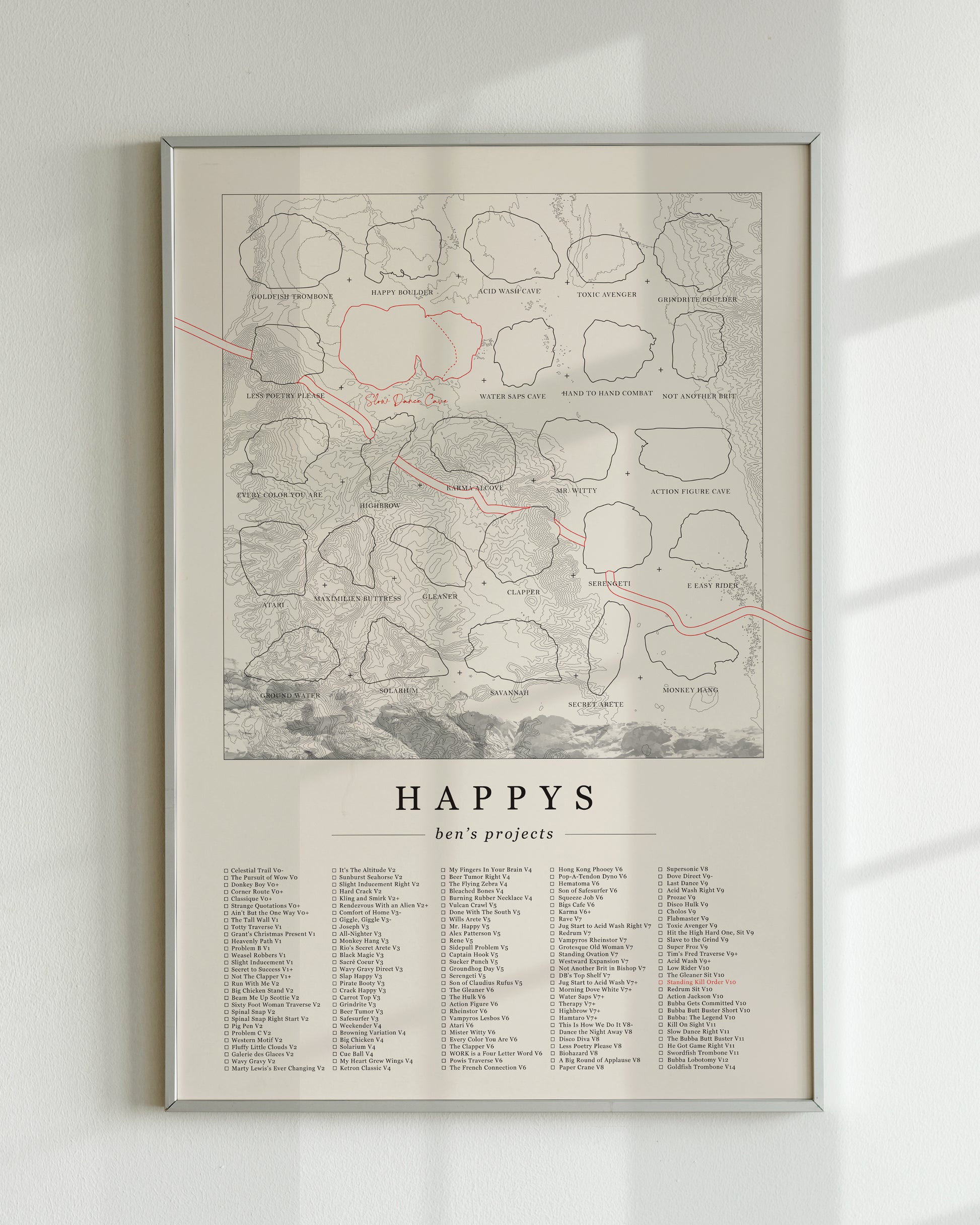 A cream color, customized rock climbing ticklist poster for the Happys rock climbing location in Bishop, California. The design has an overlay of crag topography, nature landscapes, and traced boulders, the person's name, and a list of bouldering problems at the bottom. Displayed as wall art in a living room.