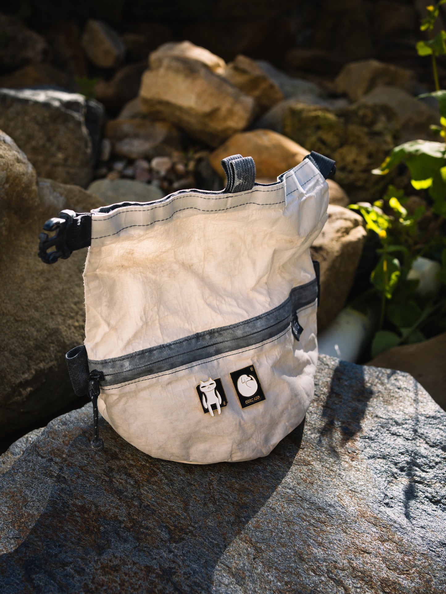 The Hitorii Napping Gou and Crashpad Mao metal chalkbag pins shown on a white and black chalk bucket.