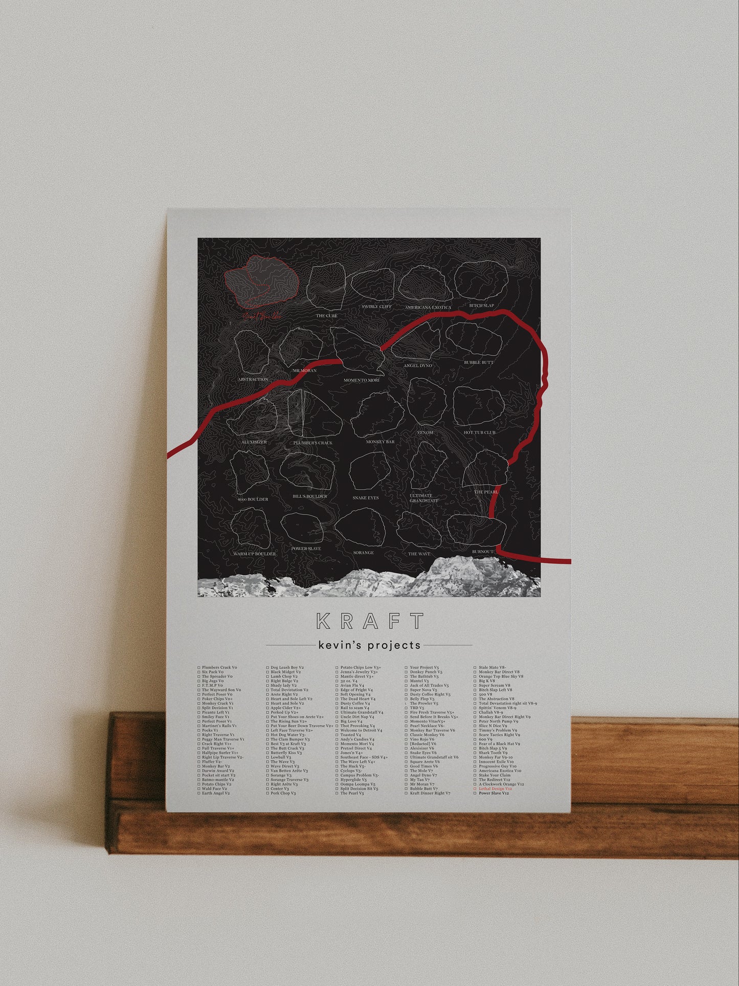 A black color, customized rock climbing ticklist poster for the Kraft rock climbing location at the Red Rocks in Las Vegas, Nevada. The design has an overlay of crag topography, nature landscapes, and traced boulders, the person's name, and a list of bouldering problems at the bottom. Displayed as wall art in a living room.