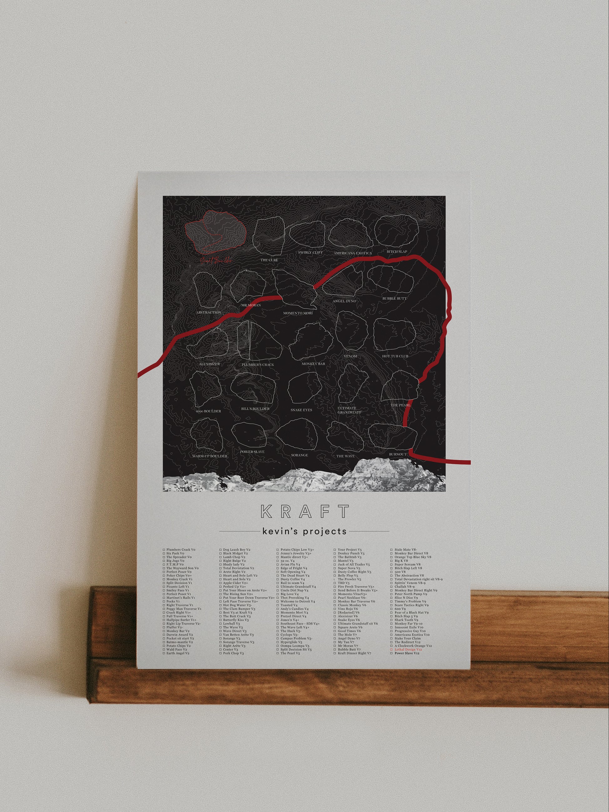 A black color, customized rock climbing ticklist poster for the Kraft rock climbing location at the Red Rocks in Las Vegas, Nevada. The design has an overlay of crag topography, nature landscapes, and traced boulders, the person's name, and a list of bouldering problems at the bottom. Displayed as wall art in a living room.