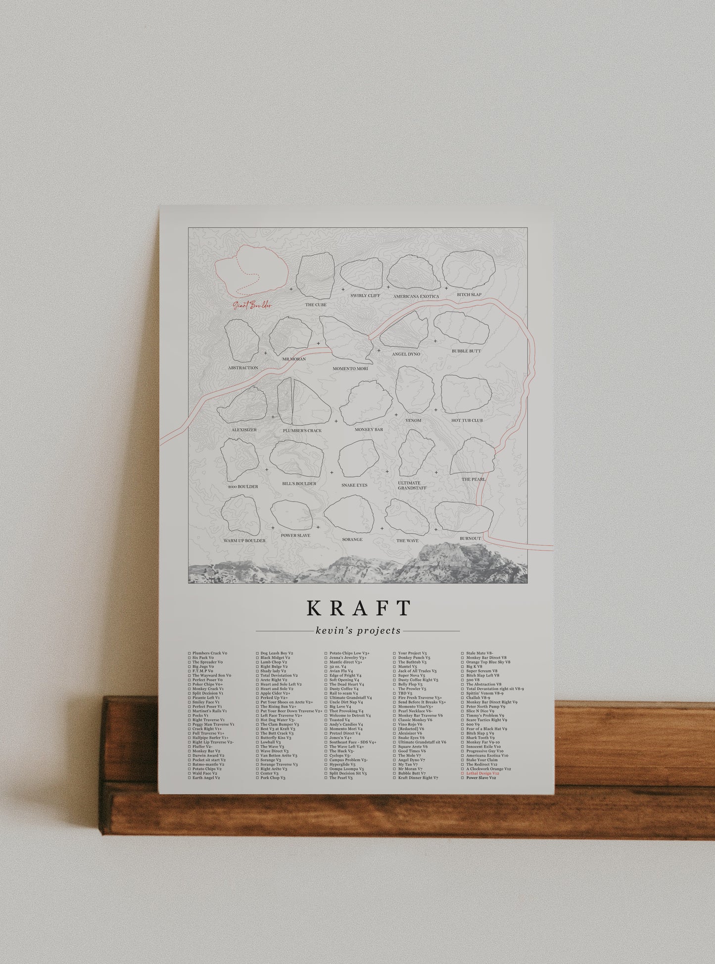 A cream color, customized rock climbing ticklist poster for the Kraft rock climbing location at the Red Rocks in Las Vegas, Nevada. The design has an overlay of crag topography, nature landscapes, and traced boulders, the person's name, and a list of bouldering problems at the bottom. Displayed as wall art in a living room.