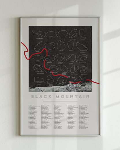 A black color, customized rock climbing ticklist poster for the Black Mountain rock climbing location in San Jacinto Mountain, California. The design has an overlay of crag topography, nature landscapes, and traced boulders, the person's name, and a list of bouldering problems at the bottom. Displayed as wall art in a living room.