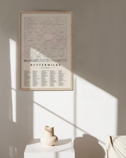 A cream color, customized rock climbing ticklist poster for the Buttermilks rock climbing location in Bishop, California. The design has an overlay of crag topography, nature landscapes, and traced boulders, the person's name, and a list of bouldering problems at the bottom. Displayed as wall art in a living room.