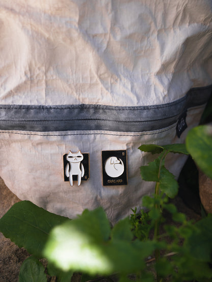 The Hitorii Napping Gou and Crashpad Mao metal chalkbag pins shown on a white and black chalk bucket.